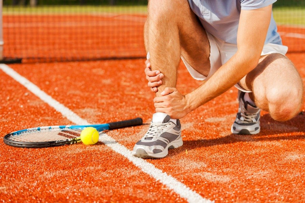 Close-up of tennis player touching his leg while sitting on the tennis court