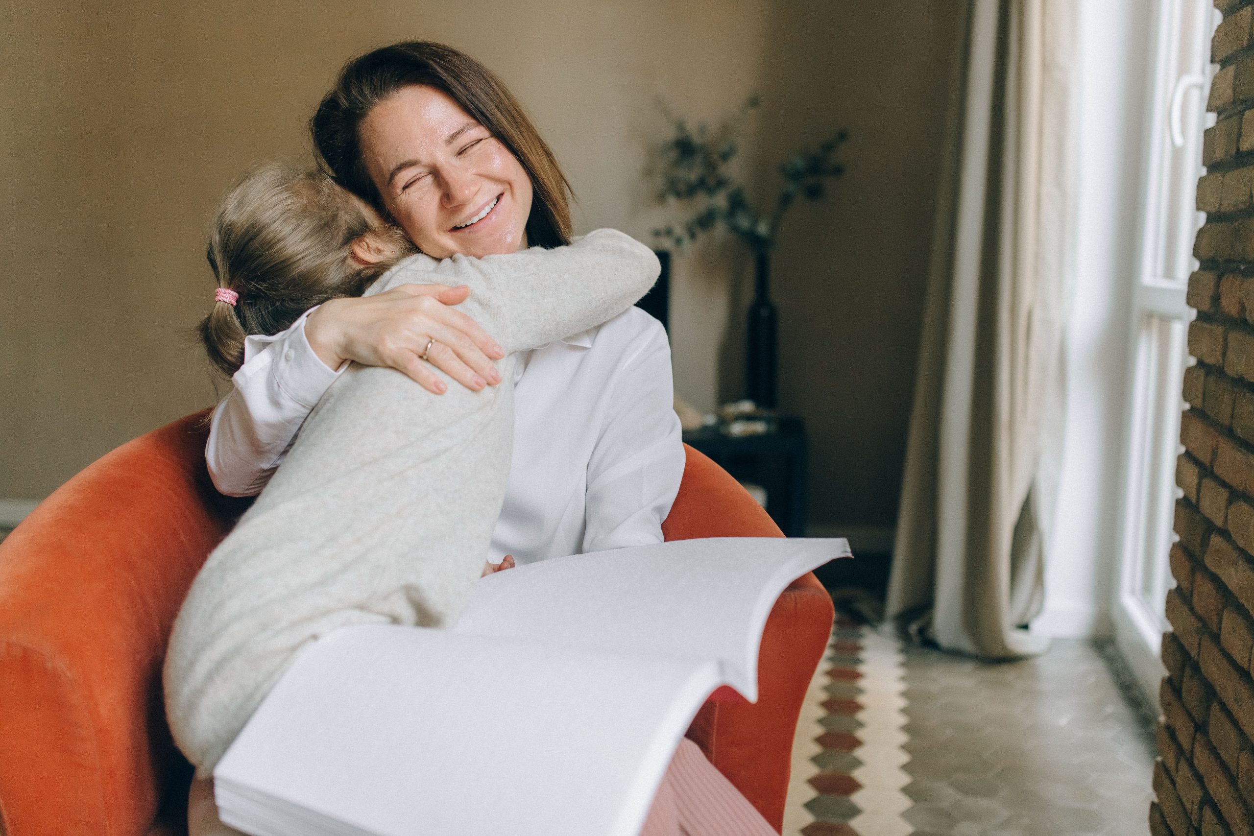 mother hugging her daughter while holding a book